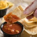 A person holding a chip with Rosarita medium green chile salsa in it over a bowl of salsa.