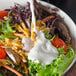 A bowl of salad with lettuce, cheese, and tomatoes with a cup of Ken's Buttermilk Ranch dressing being poured on top.