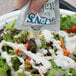 A hand pouring a Ken's Foods Creamy Italian dressing packet over a salad.