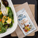 A salad in a container next to a Ken's Foods Golden Italian dressing packet.