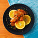 A plate of food with Sweet Baby Ray's Mango Habanero Wing Sauce and an orange slice on the table.