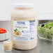 A jar of Ken's Foods creamy caesar dressing next to a bowl of salad.