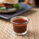 A glass cup of Ken's BBQ sauce on a table next to a burger.