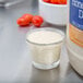 A small glass cup with a white liquid in it next to a container of cherry tomatoes.