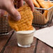 A hand dipping a potato chip into a glass of Ken's honey mustard dressing.