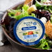 A bowl of salad with a Ken's Foods blue cheese container on a table.