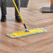 A person using a Lavex microfiber dust mop to clean a floor.