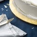 A white cake on a gold Enjay round cake drum with silverware on a blue table.