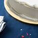 A white cake on a gold Enjay round cake drum on a blue table.