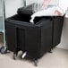 A person putting ice into a black Cambro mobile ice bin.