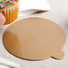 A person holding a cupcake with sprinkles on a gold and silver reversible round dessert board with a tab.