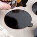 A hand holding a cupcake with a black and brown Enjay round cake board with a tab.