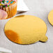 A person holding a cupcake with a yellow and black Enjay round dessert board with gold foil accents.