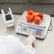 A person using a Cardinal Detecto digital price computing scale to weigh tomatoes.