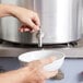 A person pouring water from a Vollrath Wear-Ever stock pot into a bowl.