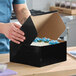 A black cake or bakery box with an open lid, containing a decorated cake inside.
