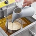 A person pouring liquid into a container using a Carnival King Funnel Cake pitcher.