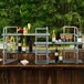 A table with Eastern Tabletop stainless steel risers and glass shelves holding bottles of wine and glasses.