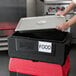 A woman using a Metro Mightylite BigBoy food pan carrier with a red and black lid to hold a tray of food.