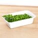 A white Pactiv Newspring microwavable container filled with green peas on a table.