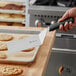 A hand holding a Mercer Culinary square edge turner over a tray of cookies.