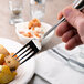 A Oneida stainless steel dinner fork being held over a plate of food.