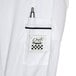 A white Chef Revival chef coat with black piping and a pen in the pocket.