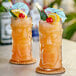 Two Anchor Hocking tiki cooler glasses with orange drinks and fruit garnish.