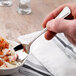 A hand holding a Oneida Needlepoint stainless steel teaspoon over a bowl of food.