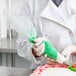 A person in a white coat using a Matfer Bourgeat standard disposable pastry bag filled with green frosting.