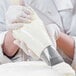 A person in white gloves using a Matfer Bourgeat disposable pastry bag to pipe frosting onto a cake.