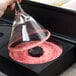 A hand using a Tablecraft glass funnel to rim a glass with pink sand.