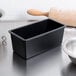 A black Matfer Bourgeat non-stick bread loaf pan on a kitchen counter next to a bowl and rolling pin.