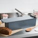 A Matfer Bourgeat long steel loaf pan with a loaf of bread on a table.