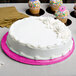 A white cake with pink frosting on a pink Enjay cake drum on a table.