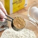 A gloved hand uses a measuring cup to scoop brown Domino Dark Brown Sugar.