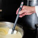 A hand holding a Matfer Bourgeat spatula with a thermometer stirring a pot of liquid.