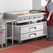 A woman using a large Cooking Performance Group gas countertop griddle to cook.