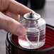 A person's hand holding a Sterno liquid candle fuel cartridge over a table with sushi.