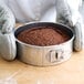 A person wearing gloves holding a brown cake in a Chicago Metallic aluminum springform cake pan.