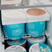 A white Avantco tub cover on a refrigerator full of ice cream containers.