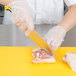 A person using a Mercer Culinary Millennia Colors yellow chef knife to cut raw meat.