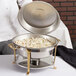 A person holding a Vollrath Classic Brass Trim Round Chafer on a table in a hotel buffet.