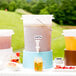A white Choice beverage dispenser with a blue base filled with a pink drink and lemons.
