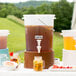 A Choice translucent beverage dispenser with brown base filled with yellow and pink drinks on a table.