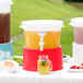 A Choice translucent plastic beverage dispenser with red base on a table with a drink in it.