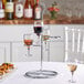 A Franmara steel wine flight stand holding wine glasses on a table.