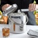 A woman using tongs to put a silver lid on a Tablecraft stainless steel ice bucket.