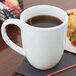 A white Tuxton Milano china mug filled with coffee on a table with a muffin.