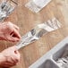 A person holding a plastic bag of forks and knives.